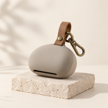 Pebble-shaped waste bag holder in mushroom-gray silicone with leather loop and brass clip